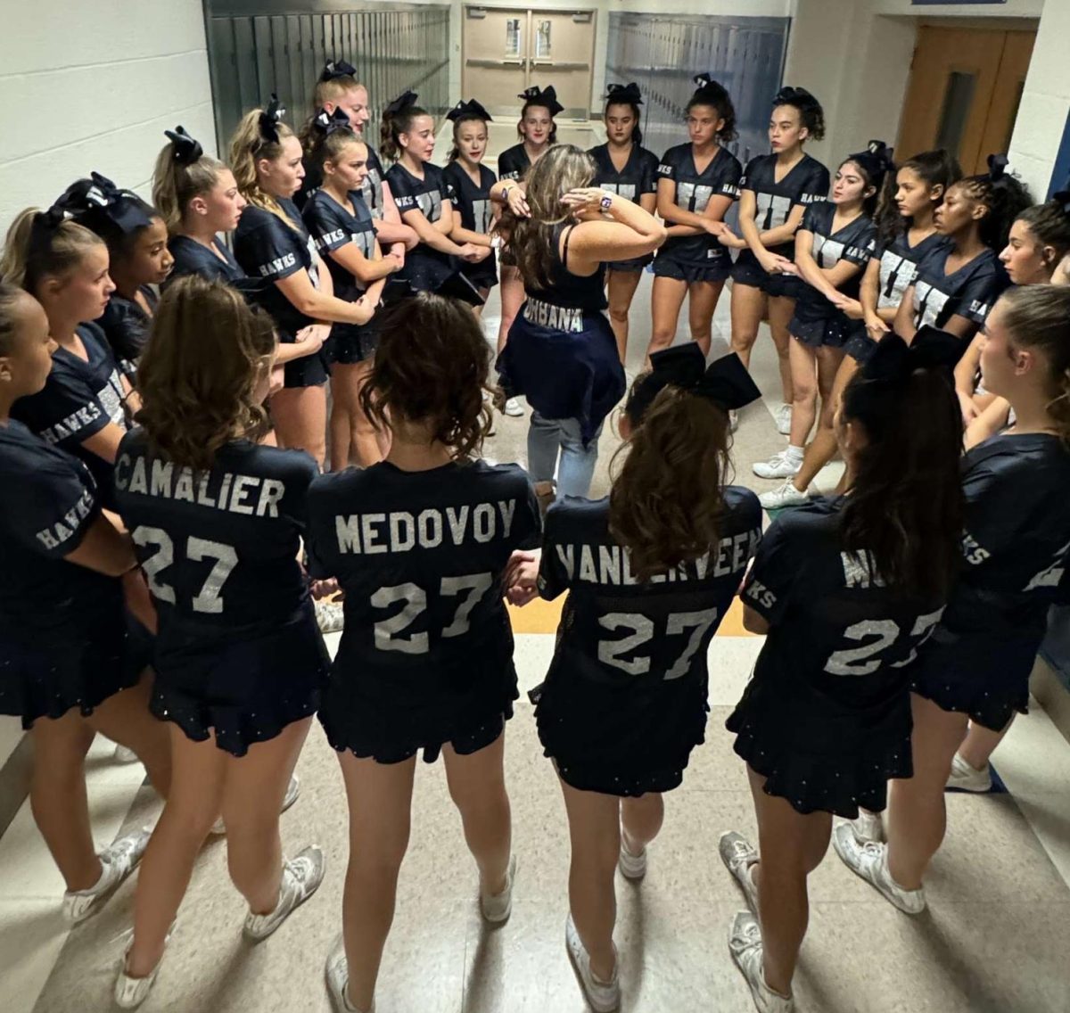 Junior Varsity Hawk cheerleaders circle around Coach K, preparing for their invitational