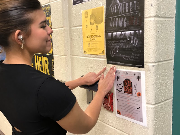 ITS Historian Bella Medina (Class of 2025) putting up a poster promoting UHS Drama's Boo Bash. The poster was designed by ITS Member at Large Claire Pettay (Class of 2026).