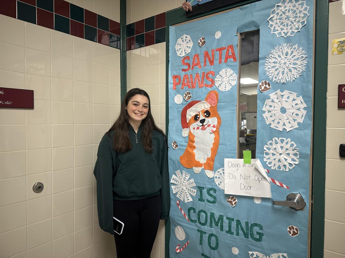 Ivy standing proudly next to her amazing decorated door, "Santa Paws is Coming to Town!"